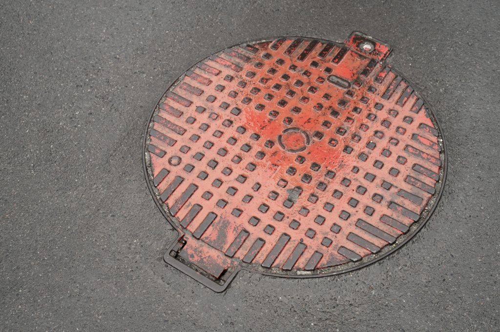 A red-painted manhole cover, set into asphalt pavement.