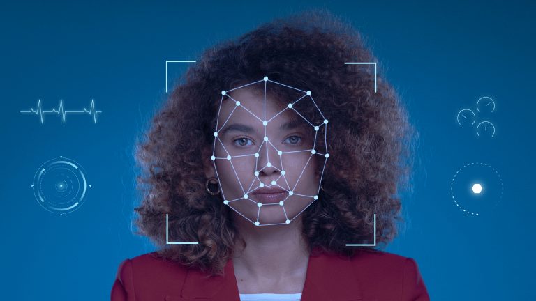 A female software developer with curly hair wearing a red blazer is facing the camera against a blue background. A digital facial recognition interface overlays her face, with geometric lines and dots mapping her facial features, and futuristic HUD-style graphics surrounding her. The image represents how AI-enhanced personality tests are used in the recruitment of software developers