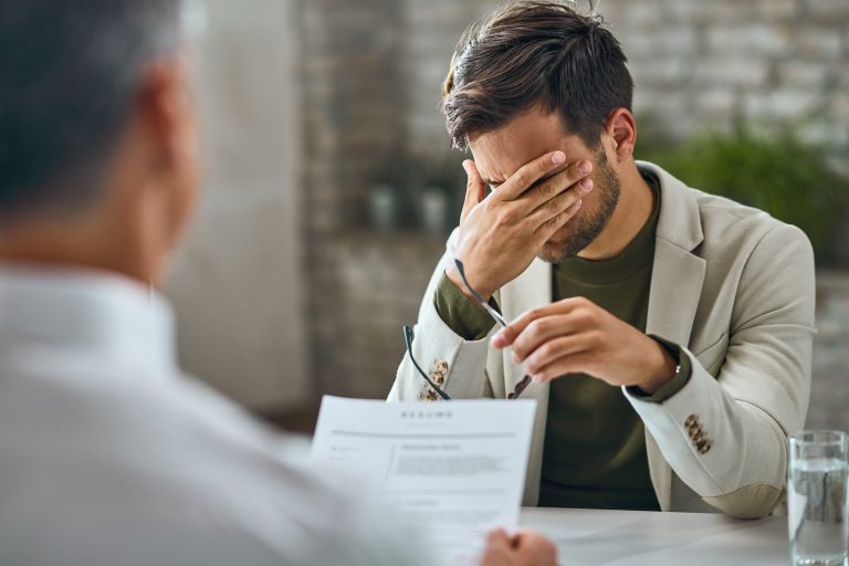 A frustrated job candidate covering his face during an interview, symbolizing red flags that software developers notice in the early stages of the hiring process