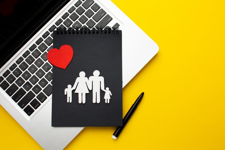 Laptop beside a family cutout and red heart, representing parental leave and work-life balance for tech workers.